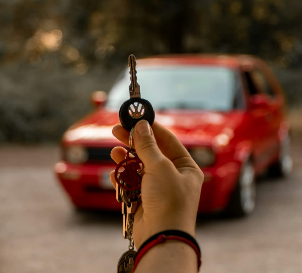 Hand holding a set of car keys with a red car in the background.
